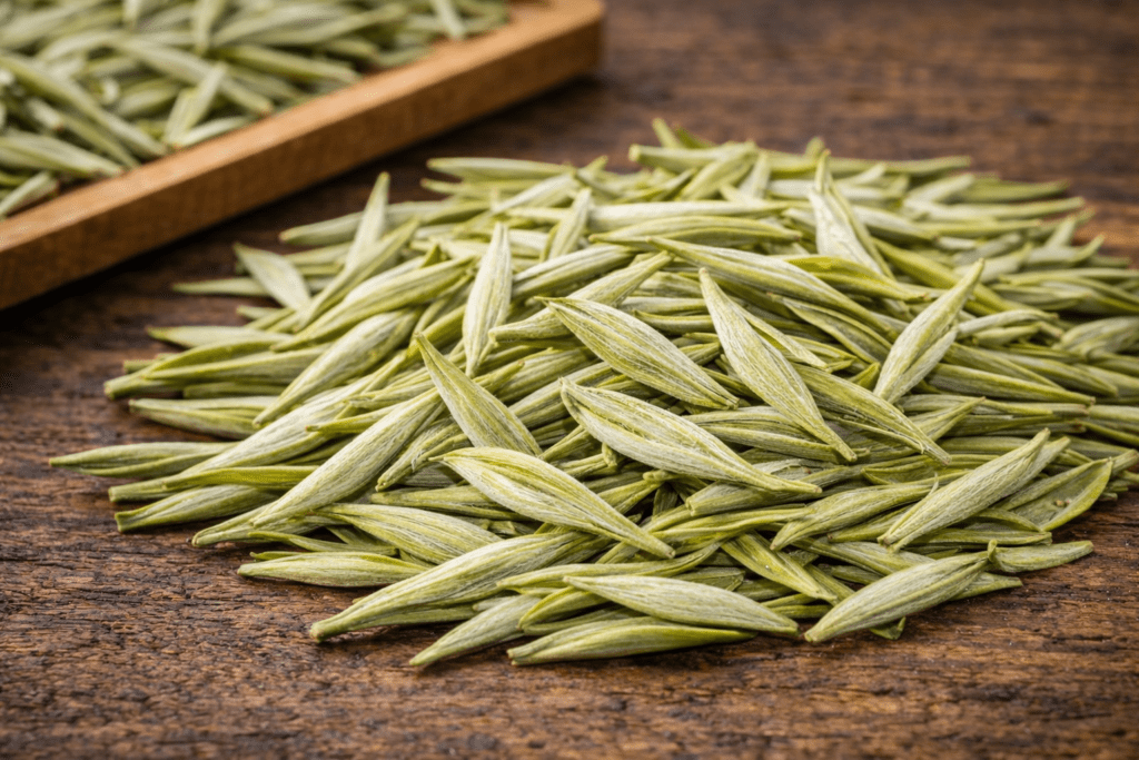 dry anji white tea leaves long flat shape on wooden table